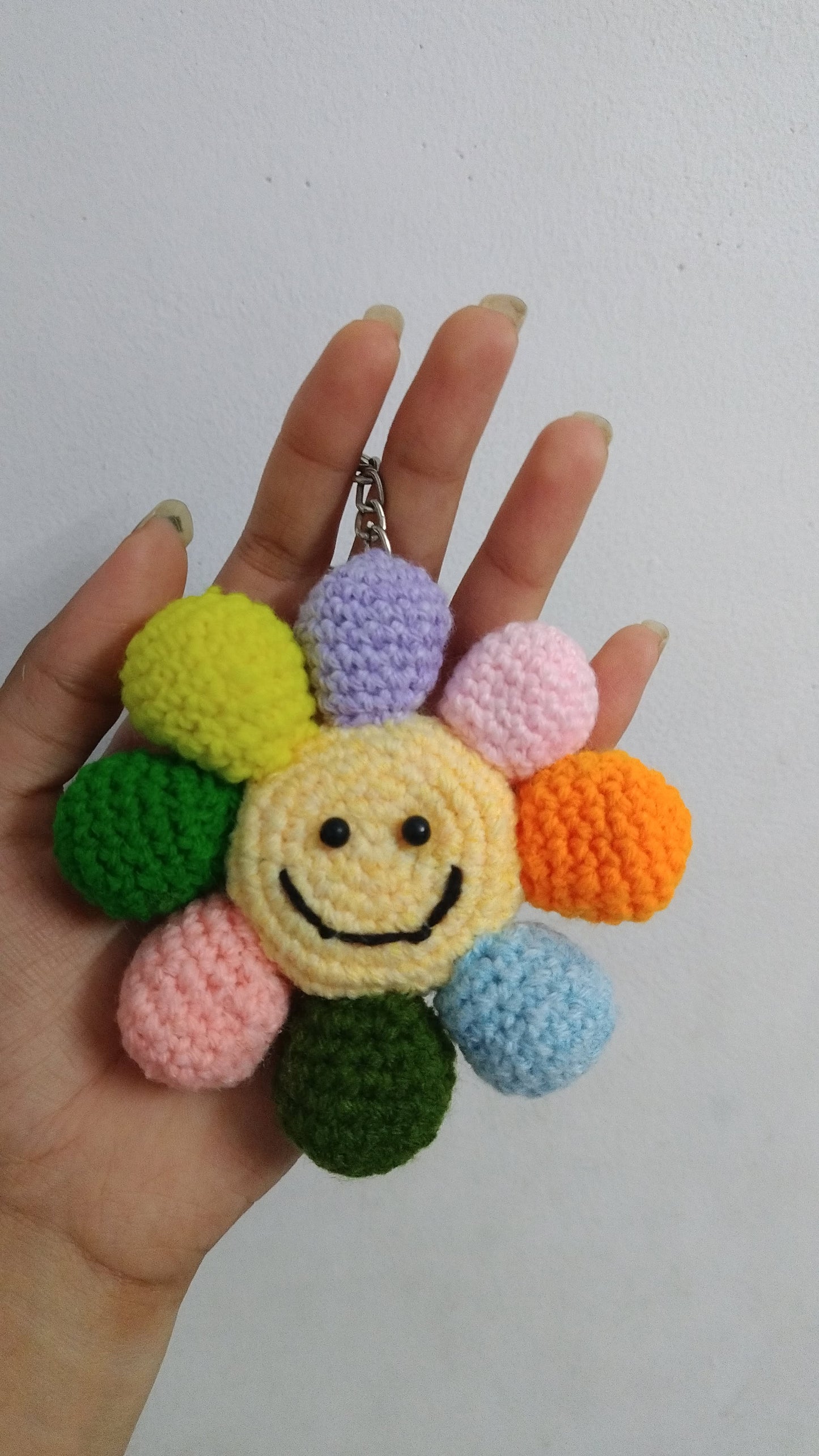 Colorful crocheted flower keychain held by a hand against a white background